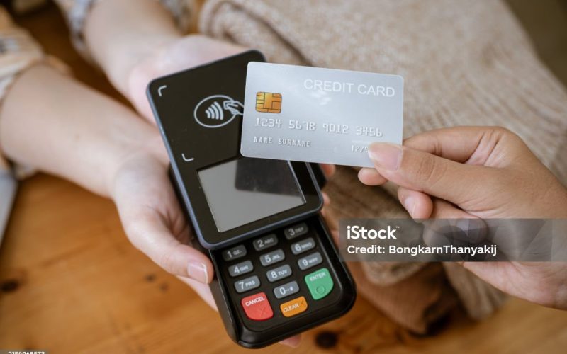 A close-up image of a customer tapping her credit card with a payment terminal or credit card machine at a cashier in a clothing store. cashless payment, card reader, electronic funds transfer